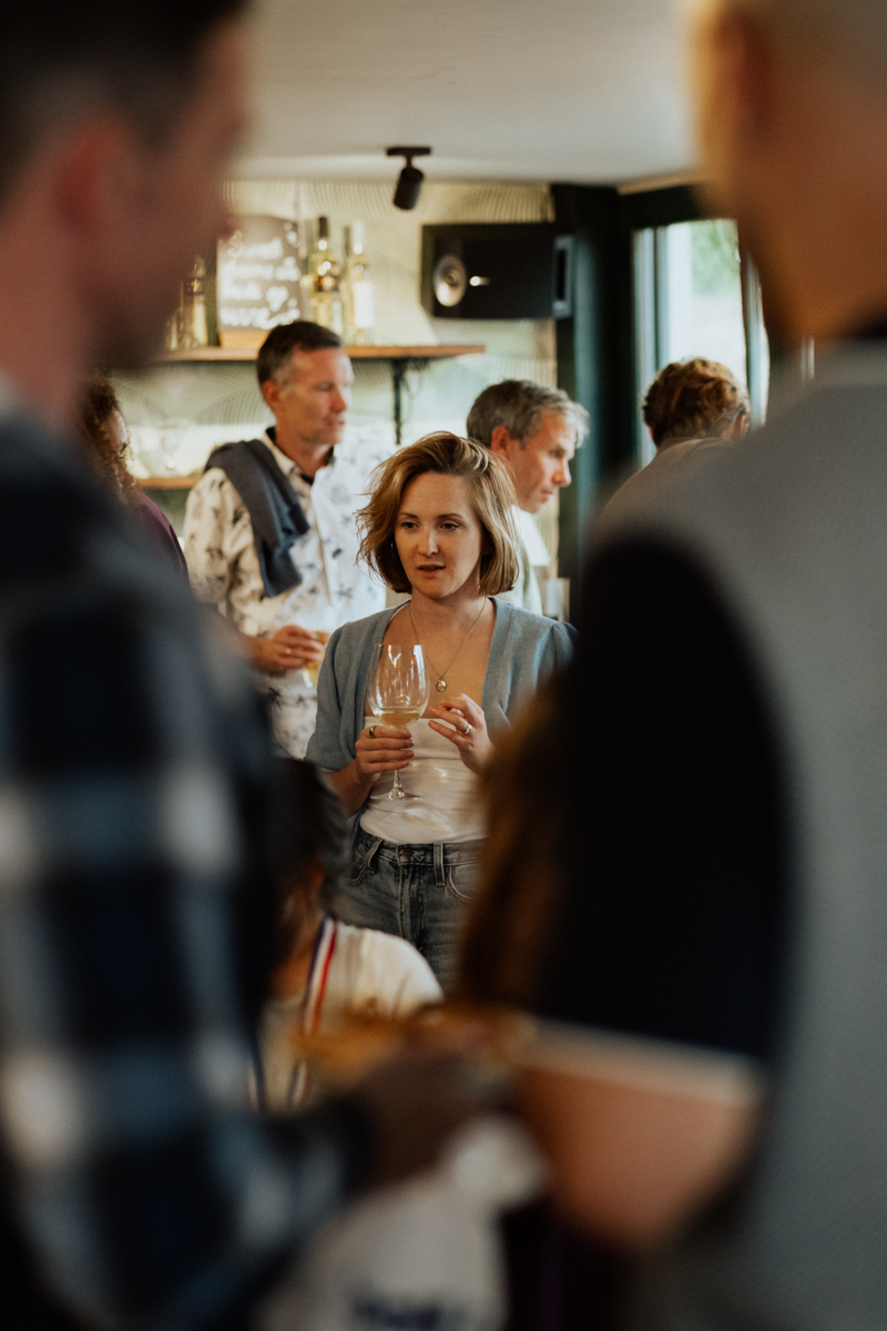 Woman holding a drink surrounded by smiling guests at London event / Frau mit Sektglas umringt von Gästen bei einer Feier in London